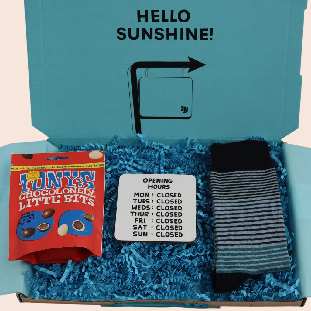 turquoise gift box with the words hello sunshine on containing Tonys chocolate, a coaster with opening hours mon to sun closed and fine blue striped socks. The packaging is plastic free with turquoise tissue with turquoise paper shred