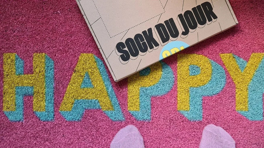 pink doormat with the words happy with feet wearing pink socks and a sock du jour letterbox gift box