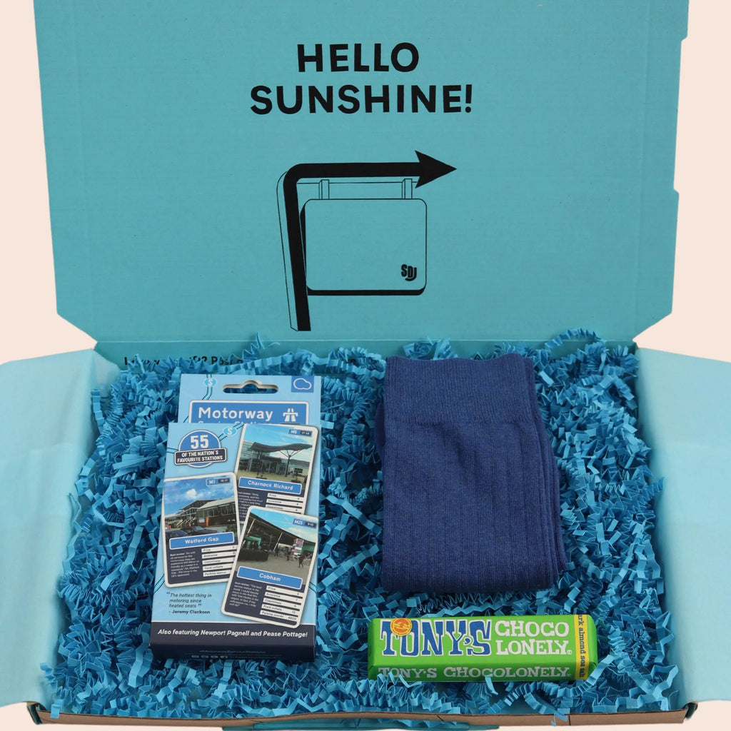 turquoise gift box with the words hello sunshine. The box contains Tonys chocolate, motorway top trumps game, and blue socks. The packaging is plastic free with turquoise tissue with turquoise paper shred