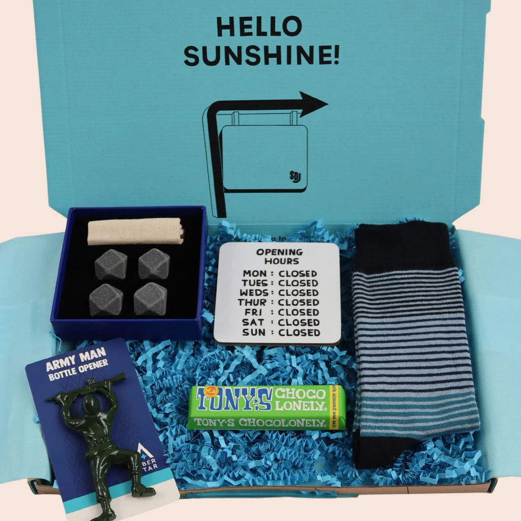 turquoise gift box with the words hello sunshine. The box contains Tonys chocolate, whisky stones, coaster with opening hours mon to sun closed, army man shaped bottle opener, and blue stripe socks. The packaging is plastic free with turquoise tissue with turquoise paper shred